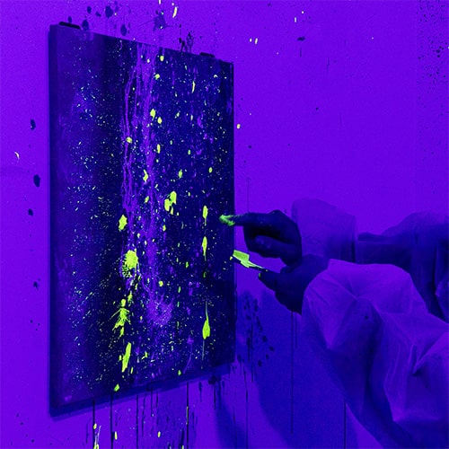 A man flicking UV painting onto a canvas with a toothbrush